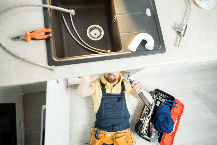Plumber laying on the ground with his head under a kitchen sink